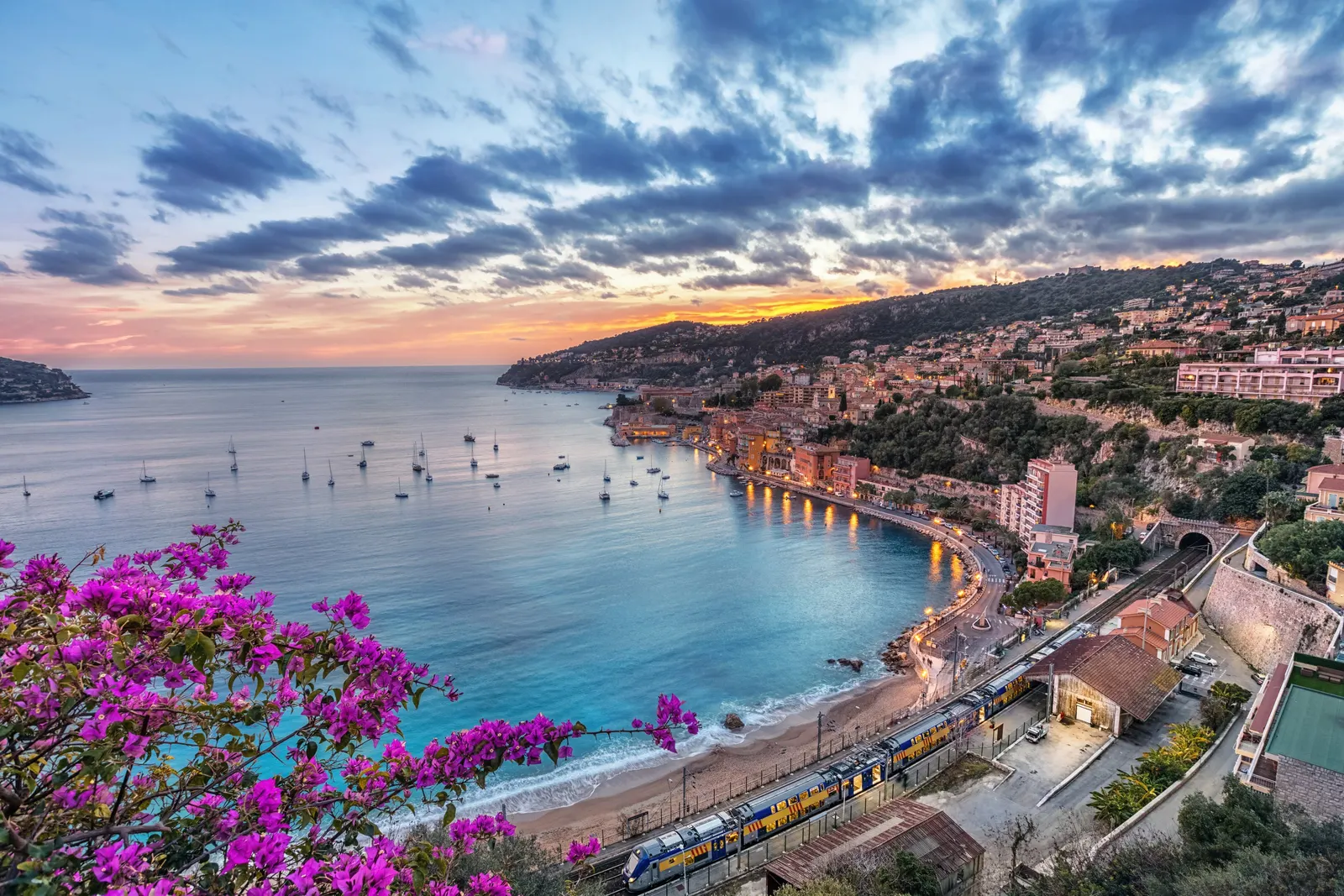 The bay of Villefranche-sur-Mer and its houses at sunset, seen from the heights through flowering bougainvillea