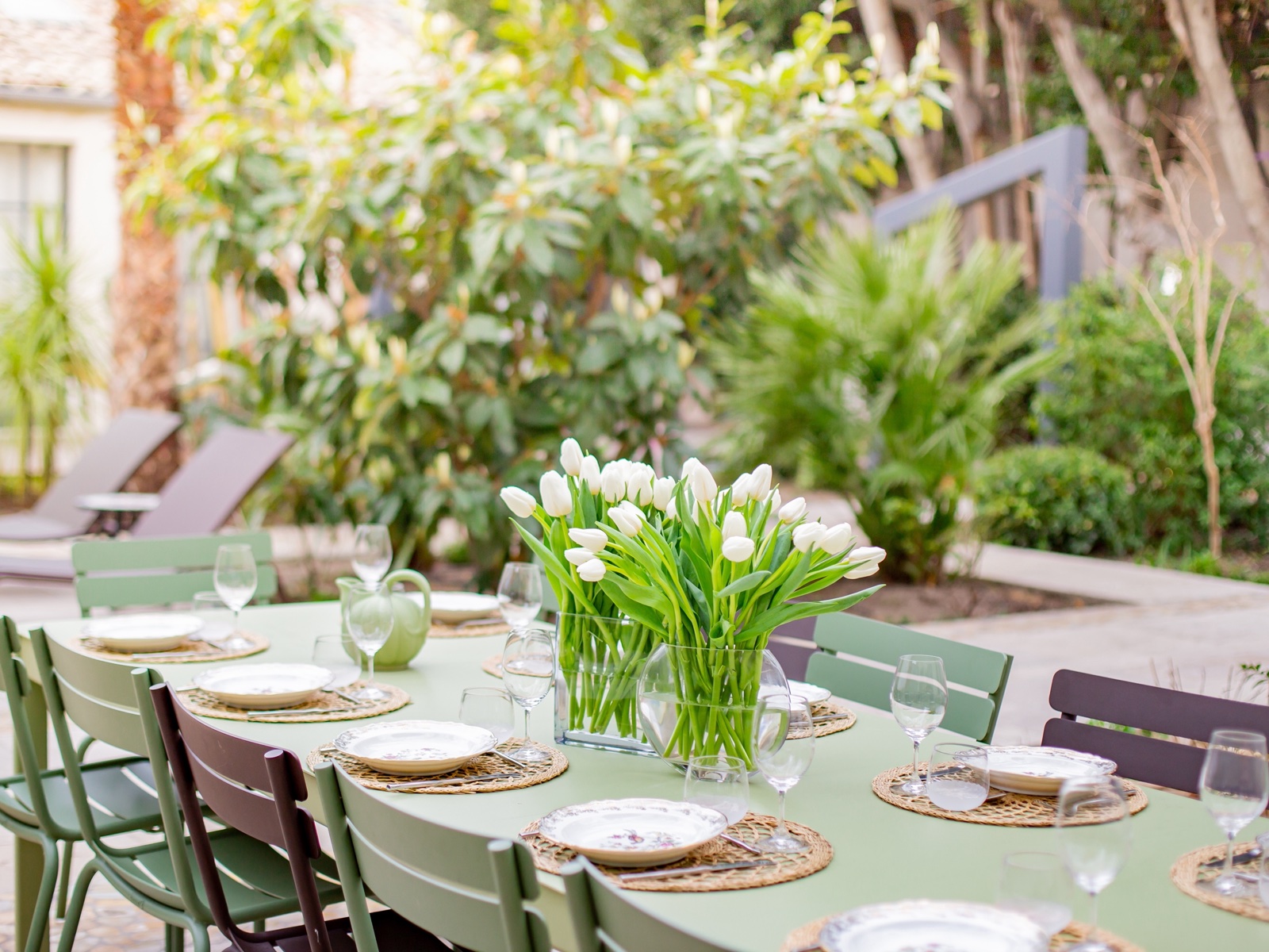 Longue table de jardin dressée pour un repas, au milieu d’un vert printanier